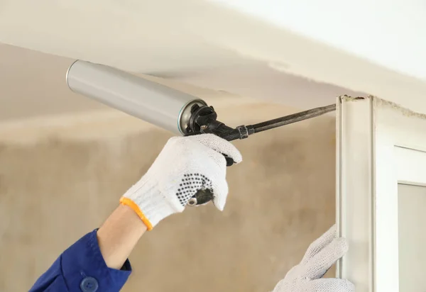 Worker using foam gun for window installation indoors, closeup