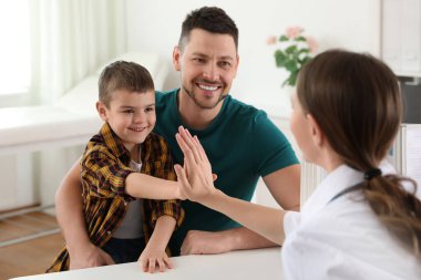 Baba ve oğul çocuk doktorunu ziyaret ediyor. Hastanede küçük bir hastayla çalışan bir doktor.