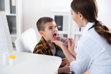 Çocuk doktoru klinikte küçük bir hastanın boğazını muayene ediyor.