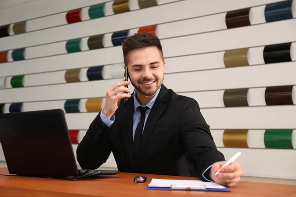 Salesman talking on phone at desk in car dealership