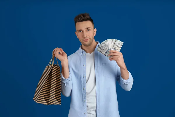 Happy man with cash money and shopping bags on blue background
