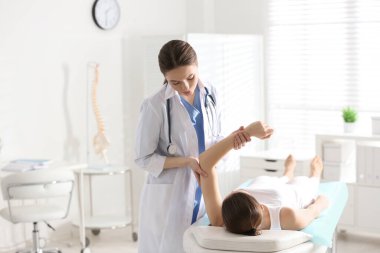 Kadın ortopedist klinikte hastanın kolunu muayene ediyor.