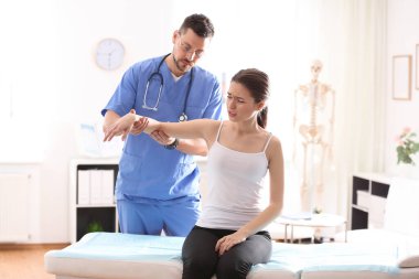 Erkek ortopedist klinikte hastanın kolunu muayene ediyor.