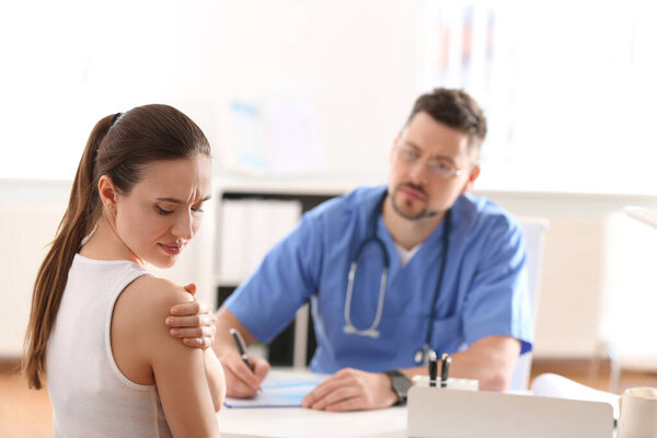 Male orthopedist examining patient with injured arm in clinic