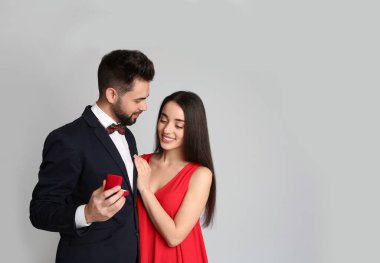 Nişan yüzüklü bir adam açık gri arka planda kız arkadaşına evlenme teklif ediyor.