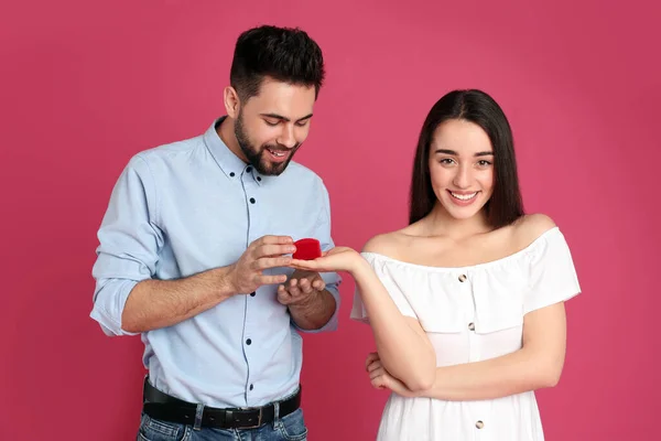 Young woman with engagement ring making marriage proposal to her boyfriend on crimson background