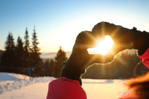 Woman making heart with hands outdoors at sunset, closeup. Winter vacation