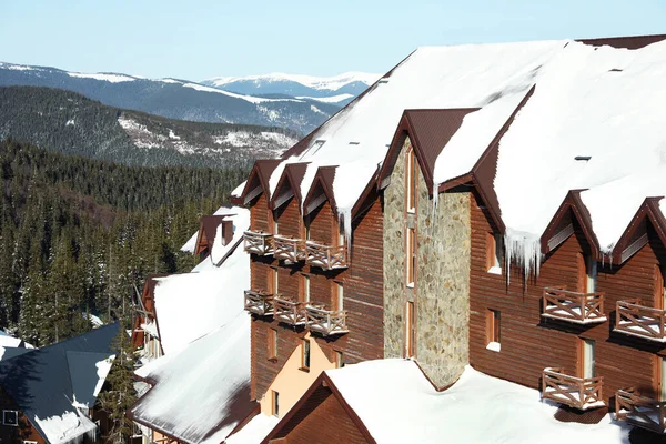 Modern cottage covered with snow in mountains on sunny day. Winter vacation