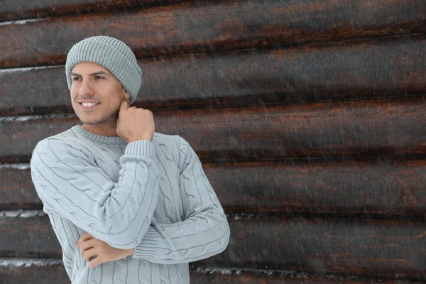 暖かいセーターと帽子を木の壁 テキストのためのスペースの近くに身に着けているハンサムな男 冬の季節 — ストック写真