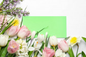 Čerstvé jarní květiny a prázdná karta na bílém pozadí, horní pohled. Mezera pro text