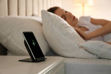 Akıllı telefon kablosuz ağlarda şarj oluyor ve kadın yatakta uyuyor.