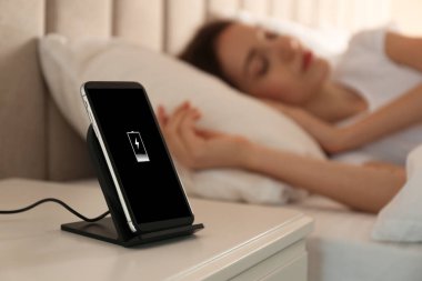 Akıllı telefon kablosuz ağlarda şarj oluyor ve kadın yatakta uyuyor.