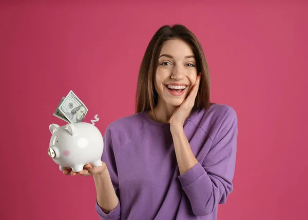 Glückliche Junge Frau Legt Geld Sparschwein Auf Rosa Hintergrund — Stockfoto