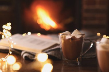 Delicious sweet cocoa with marshmallows and blurred fireplace on background clipart