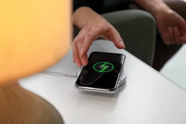 Woman taking smartphone from wireless charger in room, closeup