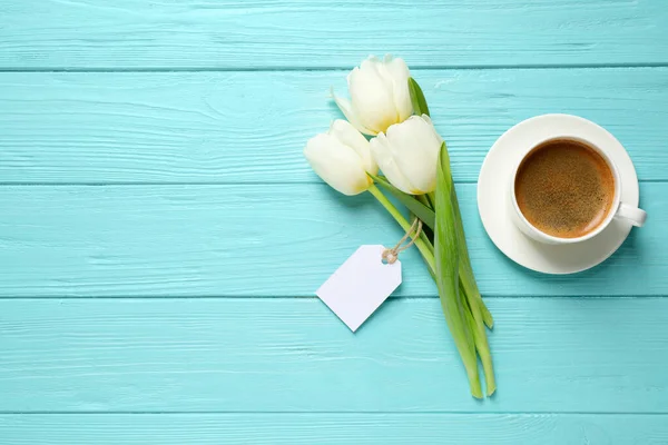 White tulips, coffee and blank tag on light blue wooden table, flat lay with space for text. Good morning