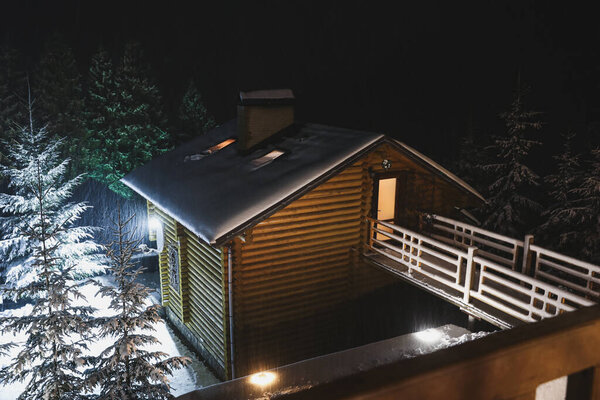 Wooden cottage with snowy yard at night, above view. Winter vacation