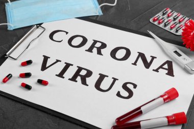 Üzerinde Corona Virüsü yazan kağıt, gri taş arka planda kan örnekleri ve ilaçlar, yakın plan.