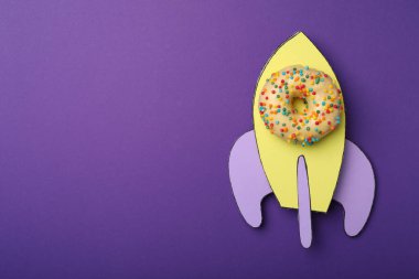 Roket, donut ve kağıttan yapılmış, mor arka plan, üst manzara. Metin için boşluk