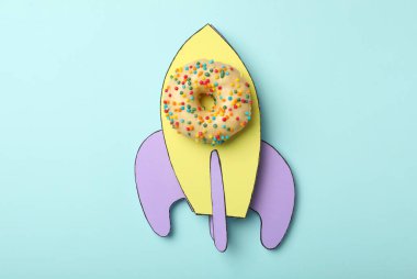 Açık mavi arka planda donut ve kağıttan yapılmış roket, üst görünüm