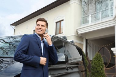 Modern bir arabanın yanında akıllı telefondan konuşan yakışıklı bir adam.