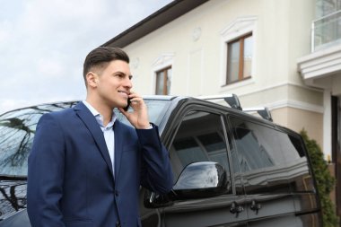 Modern bir arabanın yanında akıllı telefondan konuşan yakışıklı bir adam.