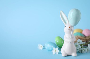 Paskalya tavşanı figürü, çiçekler ve açık mavi arka planda boyanmış yumurtalar. Metin için boşluk