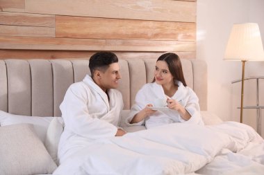 Evde yatakta kahve içen bornozlu mutlu çift.