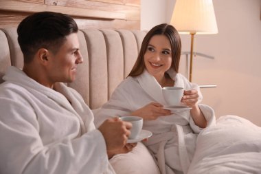 Evde yatakta kahve içen bornozlu mutlu çift.