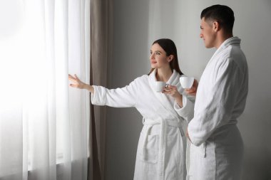 Odanın penceresinin yanında bornoz giyen mutlu çift.