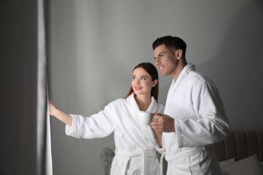 Yatak odasının penceresinin yanında bornoz giyen mutlu çift.