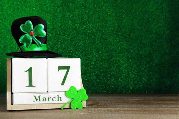 Black leprechaun hat, clover leaf and wooden block calendar on table, space for text. St. Patrick\'s Day celebration