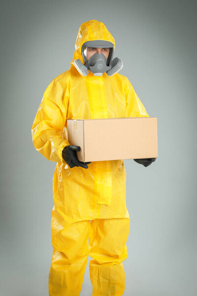 Man wearing chemical protective suit with cardboard box on light grey background. Prevention of virus spread