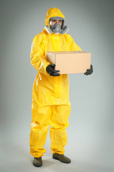 Man wearing chemical protective suit with cardboard box on light grey background. Prevention of virus spread