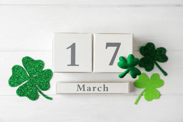 Block calendar and clover leaves on white wooden background, flat lay. St. Patrick\'s Day celebration