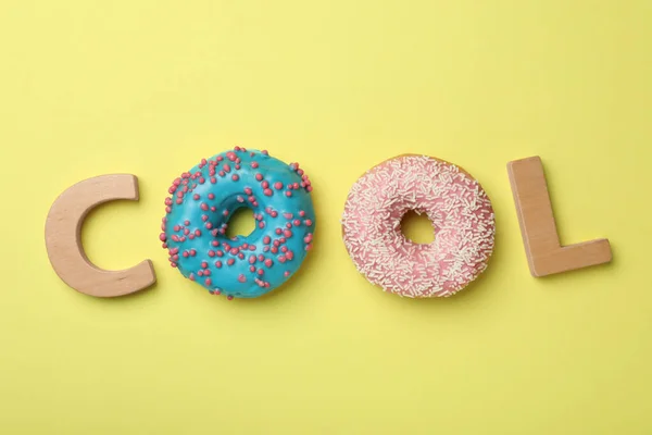 Word COOL made with wooden letters and donuts on yellow background, flat lay