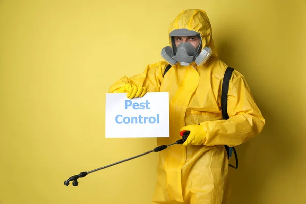 殺虫剤噴霧器保持サイン付き保護スーツを身に着けている男黄色の背景に害虫駆除 — ストック写真