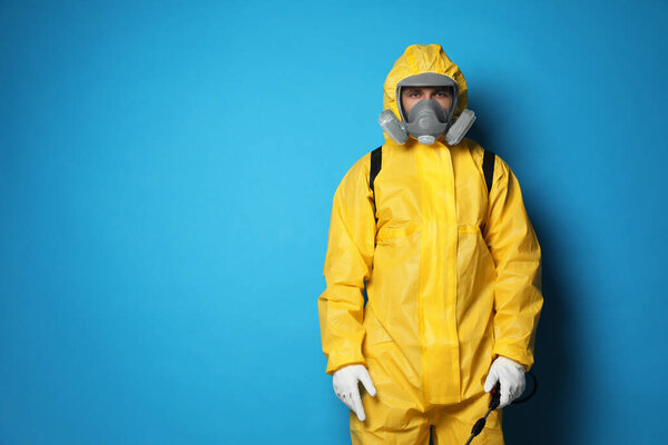 Man wearing protective suit with insecticide sprayer on blue background, space for text. Pest control