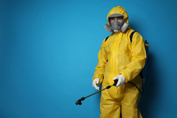 Man wearing protective suit with insecticide sprayer on blue background, space for text. Pest control