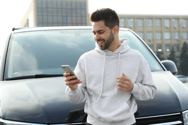 Stilig Ung Man Med Smartphone Nära Modern Bil Utomhus — Stockfoto