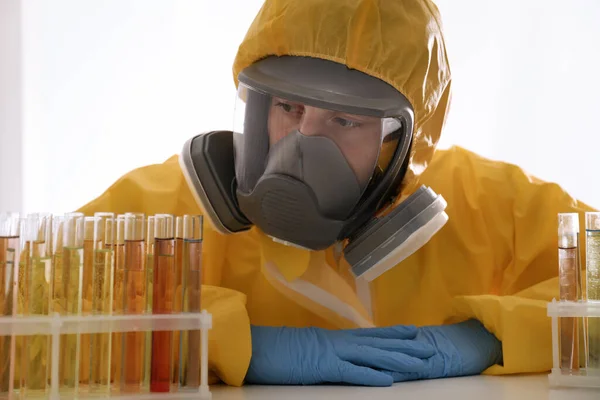 Scientist in chemical protective suit working with test tubes at table. Virus research