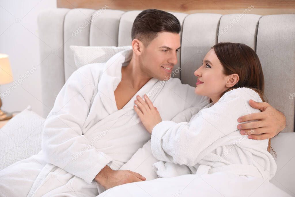 Happy couple in bathrobes resting on bed at home