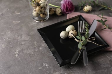 Karanlık arka planda bıldırcın yumurtası ve çiçek desenli Paskalya sofrası.