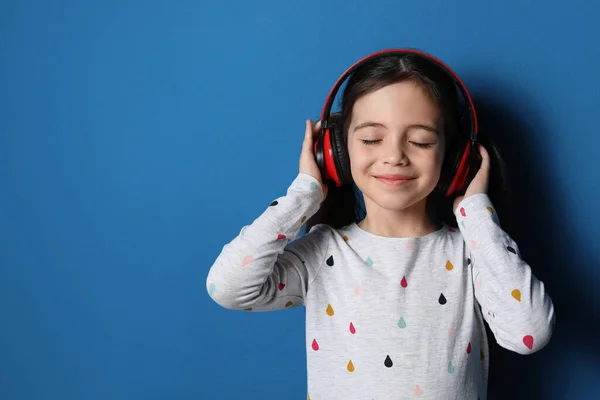可爱的小女孩带着耳机听着蓝色背景的有声读物 案文的篇幅 — 图库照片