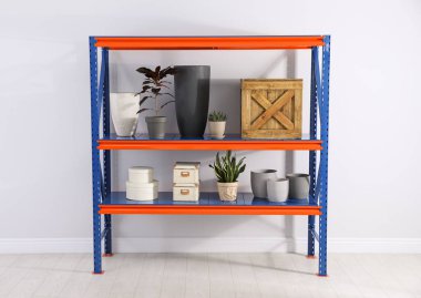 Evin içinde ışık duvarının yanında farklı ev eşyaları olan metal raf ünitesi.