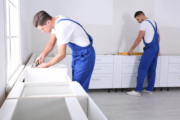 Workers installing new stylish furniture in kitchen