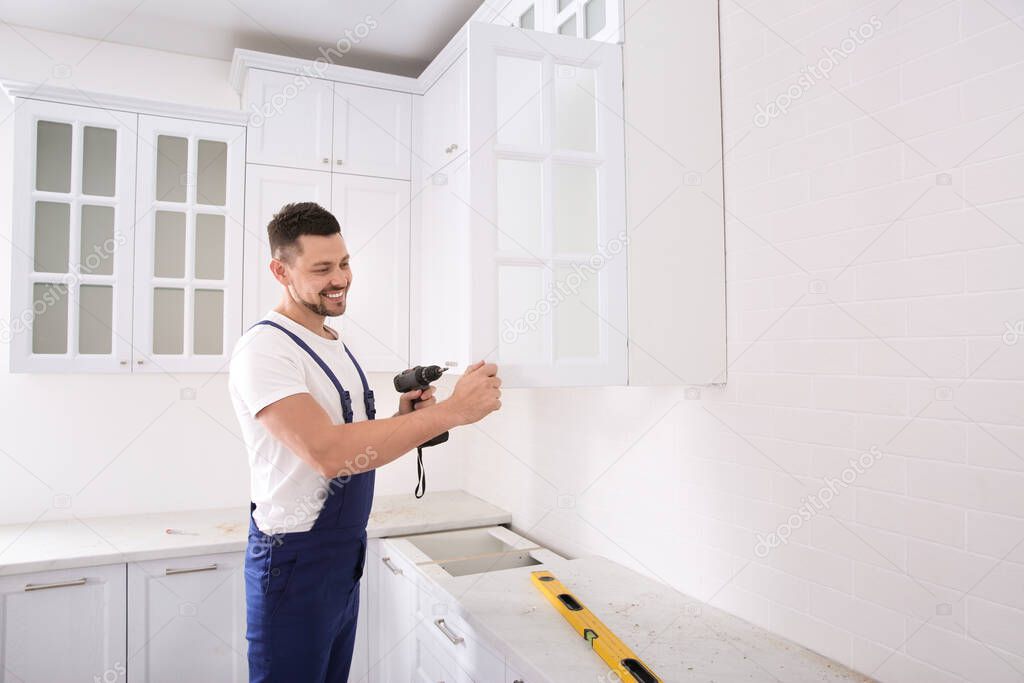 Worker installing handle on cabinet door with screw gun in kitchen