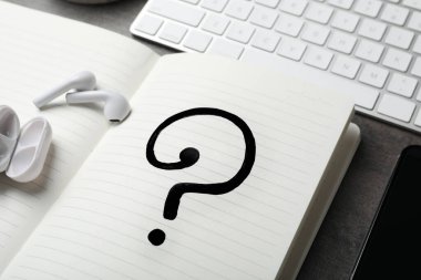 Gri masada soru işareti ve kulaklık olan defter, yakın plan.
