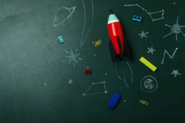 Parlak oyuncak roketi, okul malzemeleri ve karatahtadaki çizimler, düz konum. Metin için boşluk