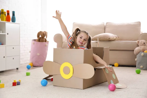 Cute little child playing with cardboard plane at home